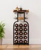 A wine rack shaped like a bottle, filled with wine bottles, sits against a white wall next to a potted plant. Anteprima dell’immagine prodotto