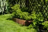 A garden scene with a wooden border separating a lawn from plants and a fence. Podgląd zdjęcia produktu