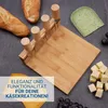 A cheese cutting board set with knives, bread, cheese, and grapes on a dark surface. Produktbild-Vorschau