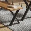 A close-up view of a wooden bench with black X-shaped legs, placed on a patterned rug in a room. Anteprima dell’immagine prodotto
