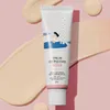 A tube of sunscreen is shown against a pink and beige background with swatches of cream. Náhled obrázku produktu