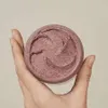 A hand holding a jar of pink cosmetic product. Produktbild-Vorschau