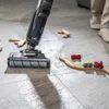 A vacuum cleaner is cleaning up a spill on a tiled floor, with a wooden toy train set nearby. Voir les images du produit