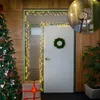 A Christmas tree and gifts are placed next to a door decorated with lights and a wreath. Produktbild-Vorschau