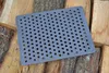 A rectangular cast iron grate with many holes lies on a pile of chopped wood. Produktbild-Vorschau
