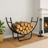 A modern black metal firewood rack filled with logs, placed next to a fireplace with a fire burning and a set of fireplace tools. Podgląd zdjęcia produktu