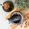A mortar and pestle filled with peppercorns, a bottle of olive oil, and a sprig of rosemary on a wooden cutting board. Voir les images du produit