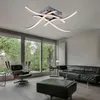 A modern living room with a sleek ceiling light, black leather sofa, and armchair, overlooking a garden through large windows. Produktbild-Vorschau