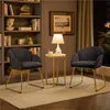 Two dark gray upholstered chairs with gold metal legs are placed in a room with a bookshelf and a side table with a lamp. Podgląd zdjęcia produktu