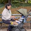 A woman is sitting on a park bench, feeding a baby in a stroller. Náhled obrázku produktu