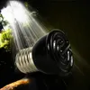 A black ceramic heat lamp bulb is placed on a dark surface, with rays of light shining down from above, suggesting a natural or terrarium environment. Podgląd zdjęcia produktu