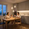 A family is having dinner at a table under a pendant light fixture in a modern kitchen. Produktbild-Vorschau