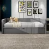 A gray daybed with pillows and a blanket is shown in a room with artwork on the wall. Produktbild-Vorschau