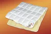 A white quilted comforter is placed on top of a yellow padded mat, both with white trim, against an orange and yellow gradient background. Produktbild-Vorschau