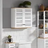 A white bathroom cabinet with wooden accents is mounted on a tiled wall, with decorative plants and other bathroom accessories visible. Náhled obrázku produktu