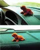 Two images of a small, orange, plush dog toy placed on the dashboard and back seat of a car. Produktbild-Vorschau