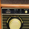 A close-up view of the control panel of a retro-style stereo system, showing various input ports and a volume knob. Náhled obrázku produktu