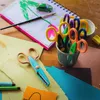 A collection of craft supplies, including scissors, paper, a notebook with a drawing, and a paintbrush, arranged on a wooden surface. Voir les images du produit