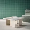 A square coffee table with a book on it, next to a fluffy chair, in front of a green grid-patterned wall. Produktbild-Vorschau