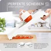 A person is using a white vegetable slicer to slice a tomato, with sliced tomatoes visible on a wooden cutting board. Podgląd zdjęcia produktu