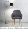 A dark gray armchair with wooden legs is placed in front of a white brick wall, next to a black floor lamp. Produktbild-Vorschau