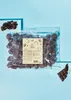 A bag of plums covered in dark chocolate, with a small pile of plums and a piece of chocolate in the foreground. Produktbild-Vorschau
