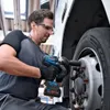A man is using a cordless impact wrench to tighten the lug nuts on a large vehicle's wheel. Podgląd zdjęcia produktu