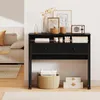 A black desk with drawers and a shelf is shown in a room with a sofa and rug. Náhled obrázku produktu
