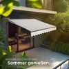 An awning is extended over a patio area next to a modern house, with lush greenery in the background. Náhled obrázku produktu