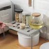 A kitchen counter with a shelf holding jars and a teapot. A hand is holding a brush. Produktbild-Vorschau