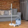 A mop and bucket set are placed on a wooden floor in front of a sofa and a brick wall. Podgląd zdjęcia produktu