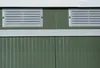 A close-up view of the upper section of a green metal storage shed, showing two ventilation grilles and white trim. Náhľad obrázku produktu