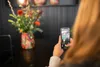 A person is taking a photo of a vase of flowers with their smartphone. Produktbild-Vorschau