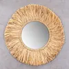 A round mirror with a woven raffia frame is displayed against a gray concrete background. Produktbild-Vorschau