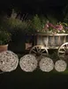 A garden scene at night with decorative light spheres in the foreground and a rustic wooden cart filled with flowers in the background. Produktbild-Vorschau