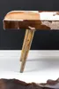 A close-up shot of a bench with a cowhide seat and wooden legs, set against a black wall and white floor. Produktbild-Vorschau