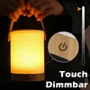 A person is holding a portable LED lamp with a fabric shade and wooden base. A close-up inset shows the touch-sensitive power button. Produktbild-Vorschau