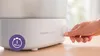 A hand is shown turning a dial on a white Philips Avent sterilizer, with a purple circular overlay indicating '10 min'. Produktbild-Vorschau