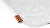 A close-up shot of a gray felt cushion with a brown leather tag attached to the corner. Produktbild-Vorschau