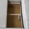 Close-up view of the open storage compartment of a sofa, showing wooden supports and a coiled strap. Produktbild-Vorschau