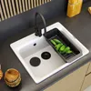 A white kitchen sink with a black faucet and a black colander filled with cucumbers. Podgląd zdjęcia produktu