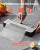A person is using a vacuum sealer machine to seal a food bag. There are vegetables and a lemon in the background. Produktbild-Vorschau