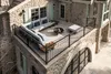A stone house with a balcony furnished with a sectional sofa, coffee table, and fire pit. Produktbild-Vorschau