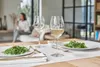 A table setting with two wine glasses and salads, with a woman blurred in the background. Anteprima dell’immagine prodotto