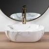 A close-up shot of a marble-patterned vessel sink with a gold faucet, set against a white and gray background with a circular mirror reflection. Podgląd zdjęcia produktu