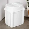 A white plastic trash can with a flip lid sits on a gray floor next to a white wall. Produktbild-Vorschau