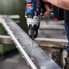 A person is using a Bosch drill to drill into a metal beam. Voir les images du produit