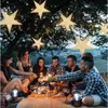 A group of friends enjoying sparklers and drinks outdoors at night, with large illuminated star decorations hanging from trees. Podgląd zdjęcia produktu