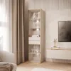 A tall, narrow display cabinet with glass doors and gold trim, filled with decorative items and books, is shown in a well-lit, modern living room setting. Produktbild-Vorschau