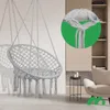 A light gray macrame hanging chair is shown suspended against a wall, with a close-up inset showing the knot detail. The chair is in a room with modern furniture and shelving. Náhled obrázku produktu